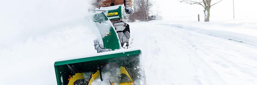 Homeowner pushes snowblower along driveway to clear out snow.